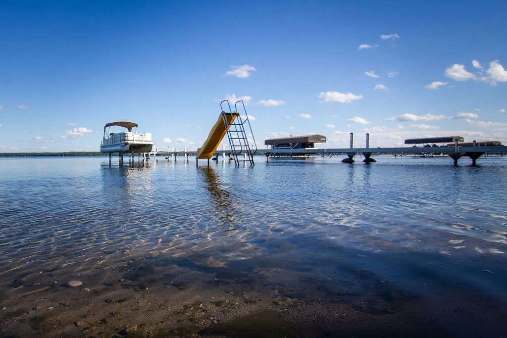 Floating swim platform with water slide and log roller on Lake Miltona under blue skies