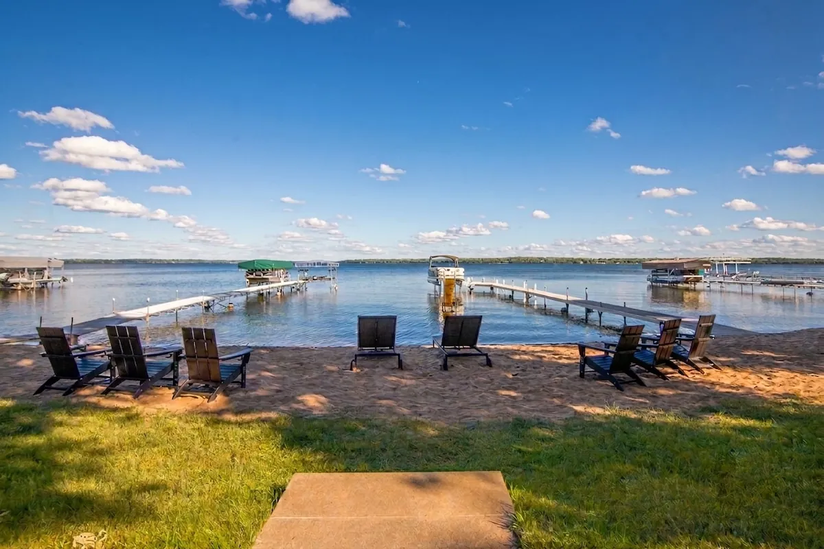 Adirondack chairs lined up on the grassy shoreline facing Lake Miltona