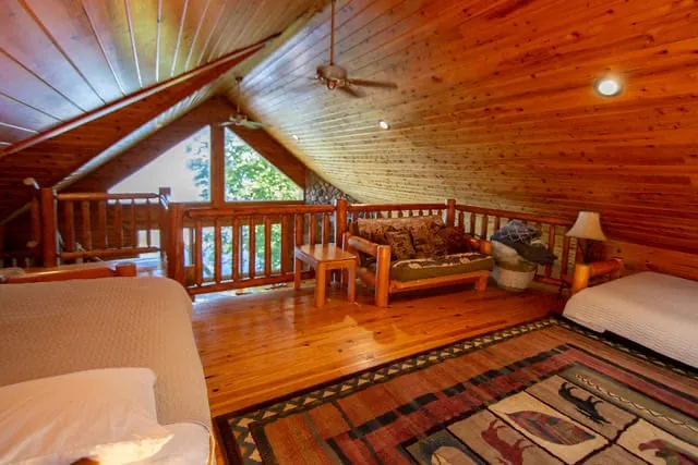 Loft overview with log railing, futon seating, and cabin rug