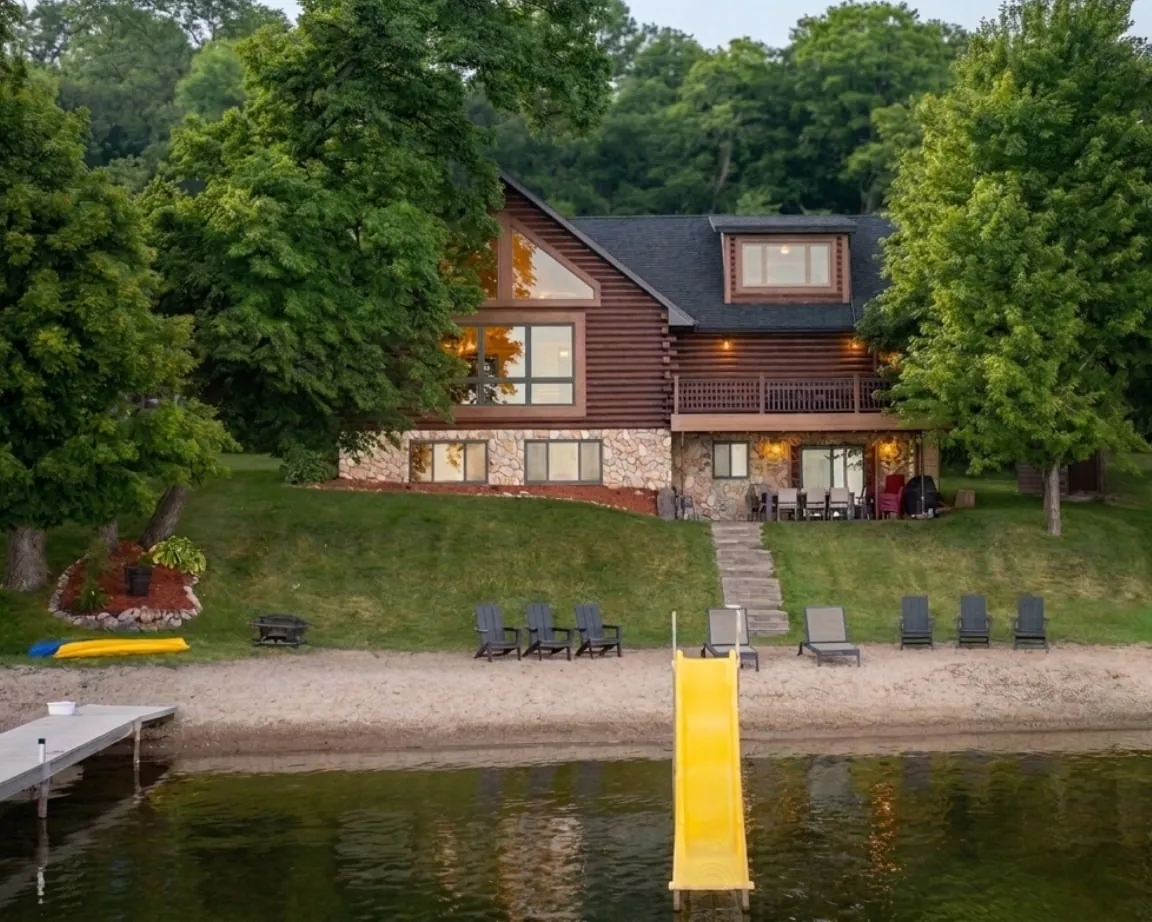 Log cabin seen from Lake Miltona with private dock, yellow slide, and shoreline chairs